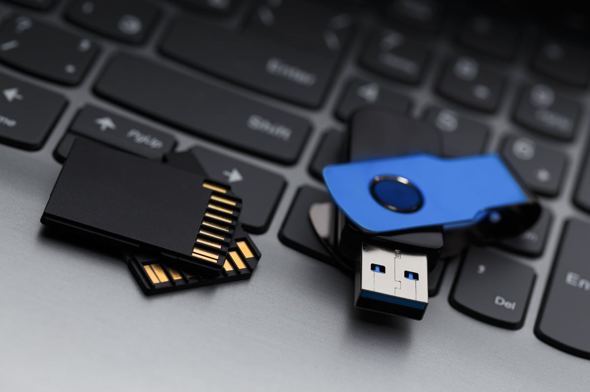 A close-up of a USB flash drive and SD memory card next to a laptop keyboard. Concept for data transfer, backup, and digital storage.