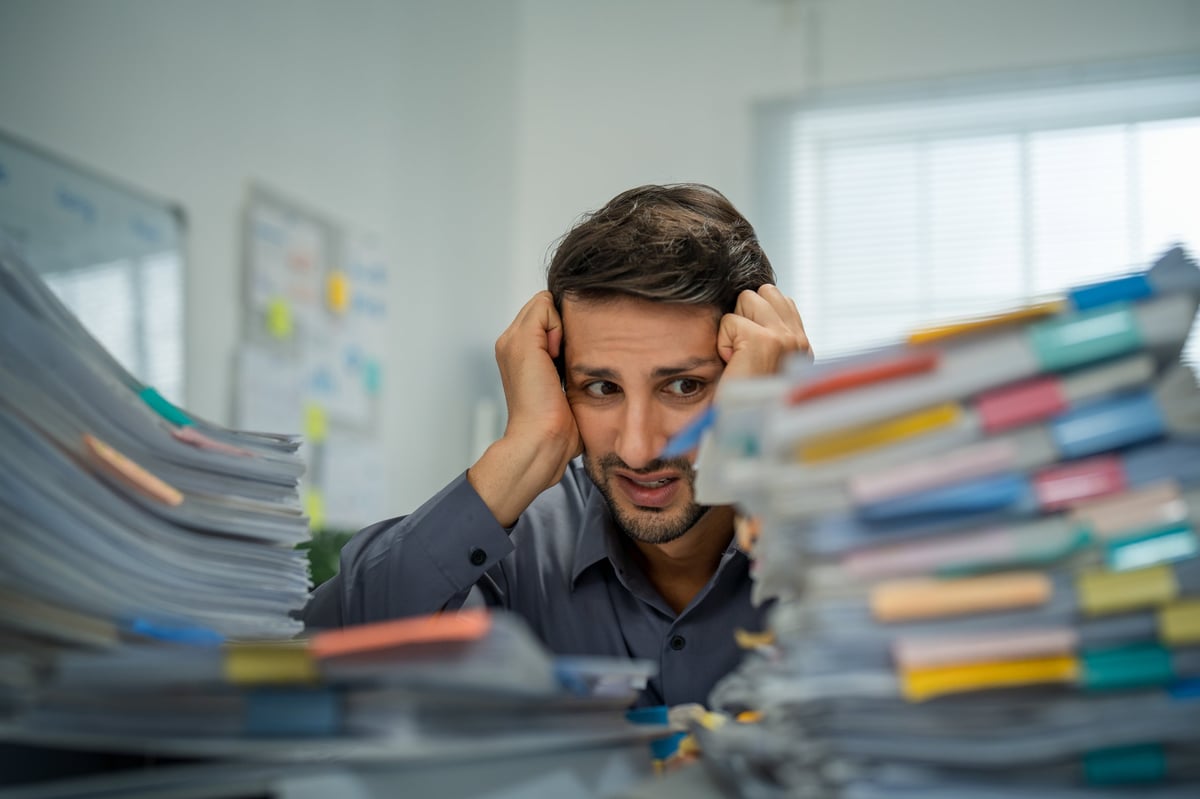 Tired Hispanic employee dealing with overwhelming workloads indoors, experiencing anxiety and pain from work-related challenges and deadlines.
